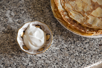 Pancakes with sour cream on kithcen table and a cat porcelain statue