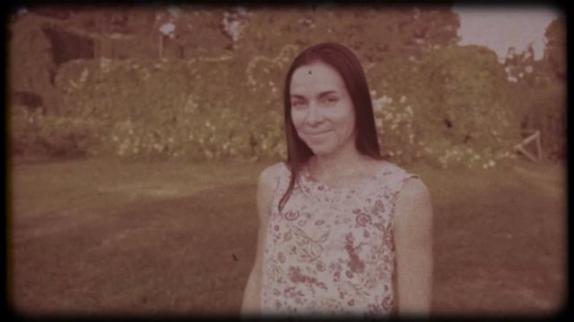 Family video archive. Retro camera 8&nbsp;mm. Old film. Young attractive woman having fun in the green garden. Portrait of a smiling brunette with dimpled cheeks against a green park. Pretty girl in summer
