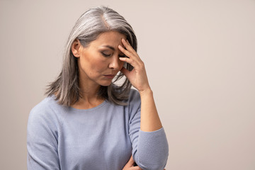 Mature Asian woman touches her forehead in distress