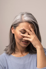 Sad Mongolian Woman with Gray Hair on a Gray Background.