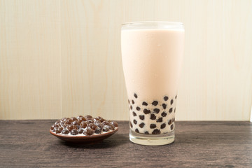 A glass cup of pearl milk tea (also called bubble tea) and a plate of tapioca ball on wooden background. Pearl milk tea is the most representative drink in Taiwan. Taiwan food . With copy space.