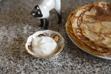 Pancakes with sour cream on kithcen table and a cat porcelain statue