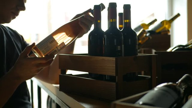Young man taking a bottle of wine from the counter at the supermarket and reading the ingredients. View from the side.