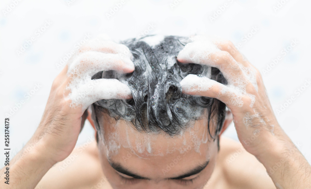 Wall mural closeup young man washing hair with with shampoo in the bathroom, health care concept, selective foc