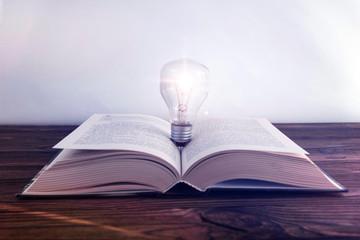Open book, light bulb on the background of a wooden table. education. creativity, business ideas.