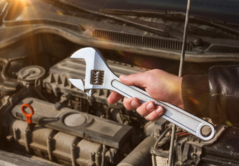 Wrench in the hand of a man on the background of the open hood of the car. repair of vehicles.