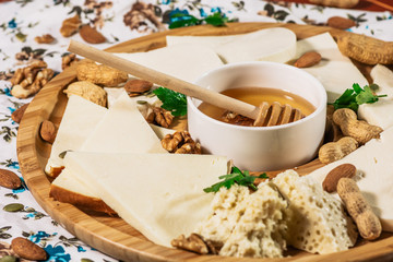 Assorted cheeses on round wooden board plate served with white wine Guda cheese, cheese grated bark of oak, hard cheese slices, walnuts, grapes, crackers, honey, sulguni, light wood background