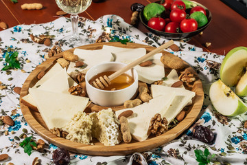 Assorted cheeses on round wooden board plate served with white wine Guda cheese, cheese grated bark of oak, hard cheese slices, walnuts, grapes, crackers, honey, sulguni, light wood background