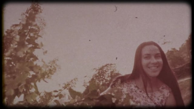 Family video archive. Retro camera 8&nbsp;mm. Old film. Young attractive woman having fun in the green garden. Portrait of a smiling brunette with dimpled cheeks against a green park. Pretty girl in summer