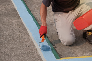 A painter painting parking lots blue lines striping in a car park.