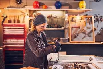 Woman carpenter sanding old window in a retro workshop.