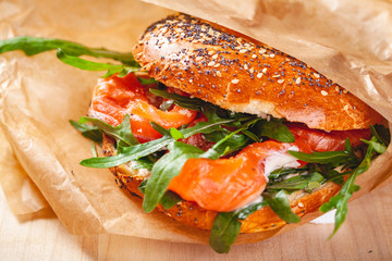 Bagel with cream cheese, smoked salmon and arugula salad in brown paper bag. Close up