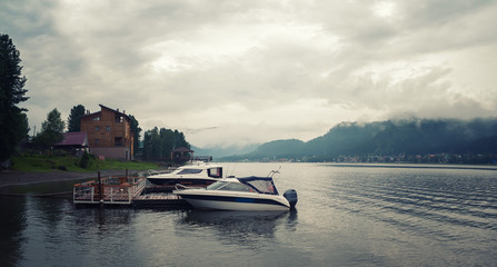 summer landscape on a mountain lake. fog over the forest and mountains.  glade two small boats near...