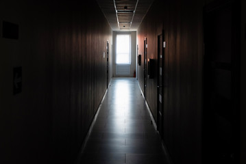 Dark corridor with doors and window light in the end