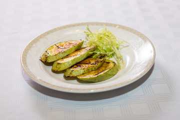 delicious fried zucchini grilled beautifully served on a platter in the restaurant,.fried zucchini in oil on a plate close-up, zucchini with toasted crust and salad on a dish