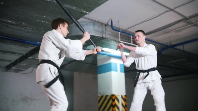 Two men in kimono training kendo on a parking lot. Sword fight