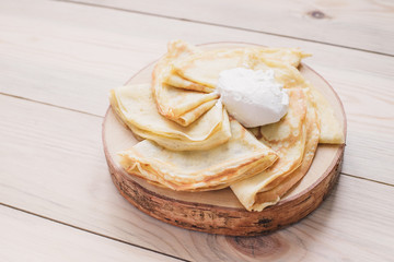 Russian thin pancakes on a wooden stand made of natural wood with sour cream . Maslenitsa is a Maslenitsa food festival.