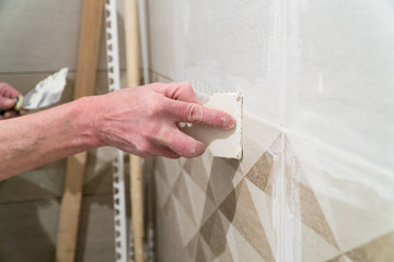 Worker with a rubber spatula fill the seams with a solution. Finishing works, blurred focus. The technology of laying tile.