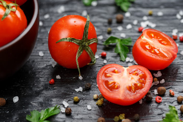 Fresh Sliced Cherry Tomatoes on a black background with spices coarse salt and herbs