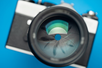 An old vintage camera. Focus on lens aperture. Blue background