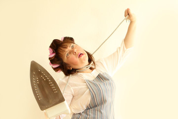 A woman with an iron cord around her neck in home clothes, in an apron, with hair curlers in her...