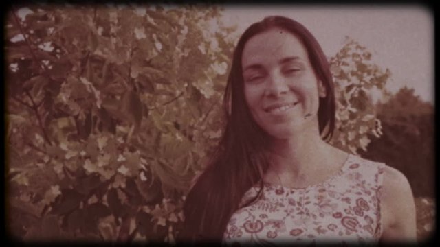 Family video archive. Retro camera 8 mm. Old film. Young attractive woman having fun in the green garden. Portrait of a smiling brunette with dimpled cheeks against a green park. Pretty girl in summer