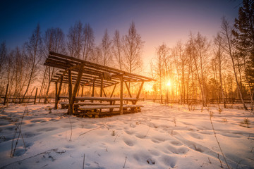 Wooden pavilion with snow in winter forest at sunrise.
