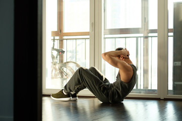 A handsome man doing plank exercises against the window of a house