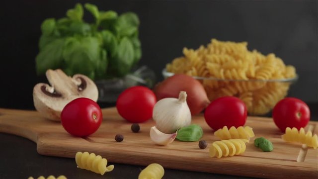 pasta ingreidents camera zoom motion .fusilli cherry tomatoes basil garlic mushroom on wooden background