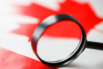 The flag of CANADA looks through a magnifying glass. Study of the history and culture and people of the country of Canada. The concept of studying the geography customs and English of Canadians