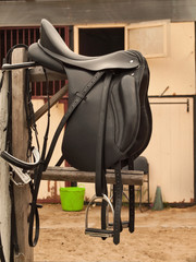 Fototapeta na wymiar Bridle and professional dressage saddle hanging near stable