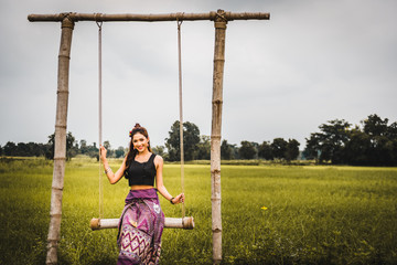 Beautiful Asian woman in local dress sitting on swing and enjoy natural on bamboo bridge in rice field