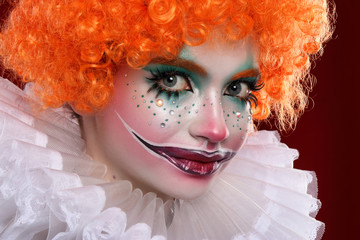 Cute red-haired clown.Girl in bright clown makeup. Close up.