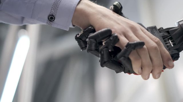 Future is now. Male hand of young student scientist inventor shakes robotic arm. Hand of a man shaking hands with robot. Robotic and human hands join in a handshake.