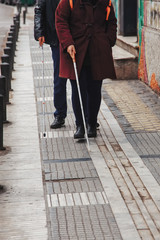 blind man and woman walking on the street using a white walking stick