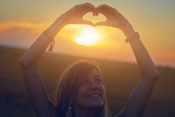 Girl holding heart-shape symbol for love in sunset / sunrise time.