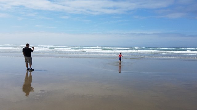 father taking picture of son in sand and water at beach