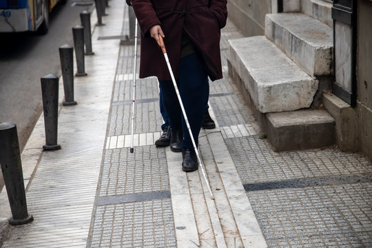 blind man and woman walking on the street using a white walking stick
