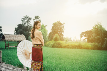Beautiful Asian woman in local dress holding paper umbrella standing and enjoy natural on bamboo bridge in rice field
