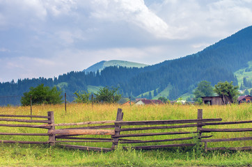 Fototapeta na wymiar wooden fence in a meadow in the mountains, houses in the background
