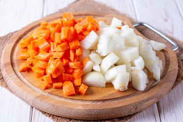 Onions and carrots chopped on a cutting board on a wooden table