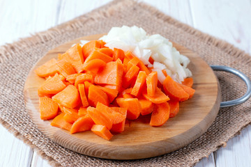 Onions and carrots chopped on a cutting board on a wooden table