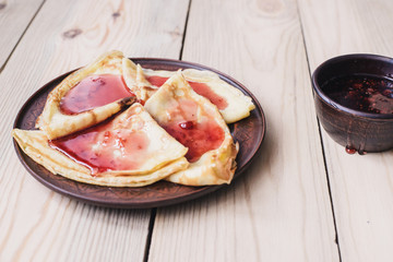 Carnival. Russian pancakes pour raspberry jam. Wooden table