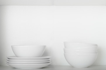 Fototapeta na wymiar White plates and bowls on a shelf in the cupboard. Kitchenware, clean dishes