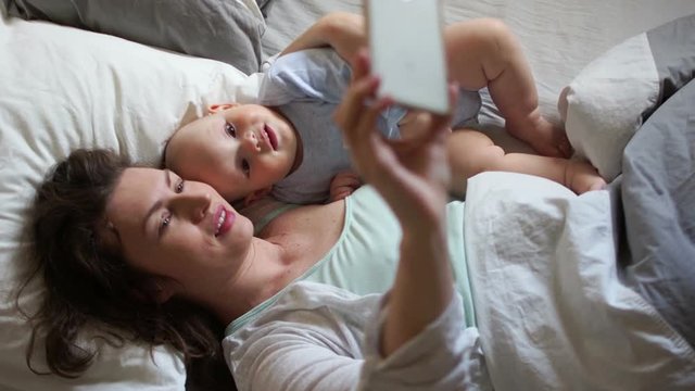 Mom and baby are lying in bed and taking selfies. Mother's day, good morning family, smartphone and baby