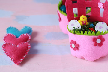 Pink and blue felt hearts near Easter basket made of pink felt with white eggs and yellow chicken in a basket. Happy Easter Day background for greeting card template, place for text. Handmade 