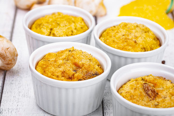 Polenta with mushrooms in white ramekin bowls on wooden rustic table. Close up