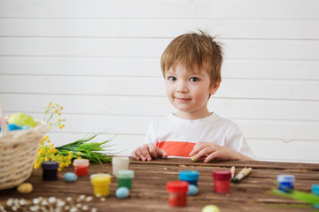 Painted and decorated eggs for Easter. Portrait of cute boy 3 years old. He holds a brush and paints Easter eggs