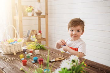 Portrait of a cute boy 3 years old. He holds brush and paints Easter eggs