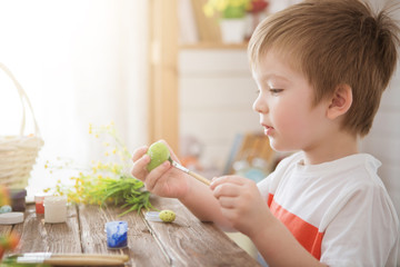 Boy holds an egg and painting with brush. Preparing for celebration of Easter. Little boy painting and decorating Easter eggs.